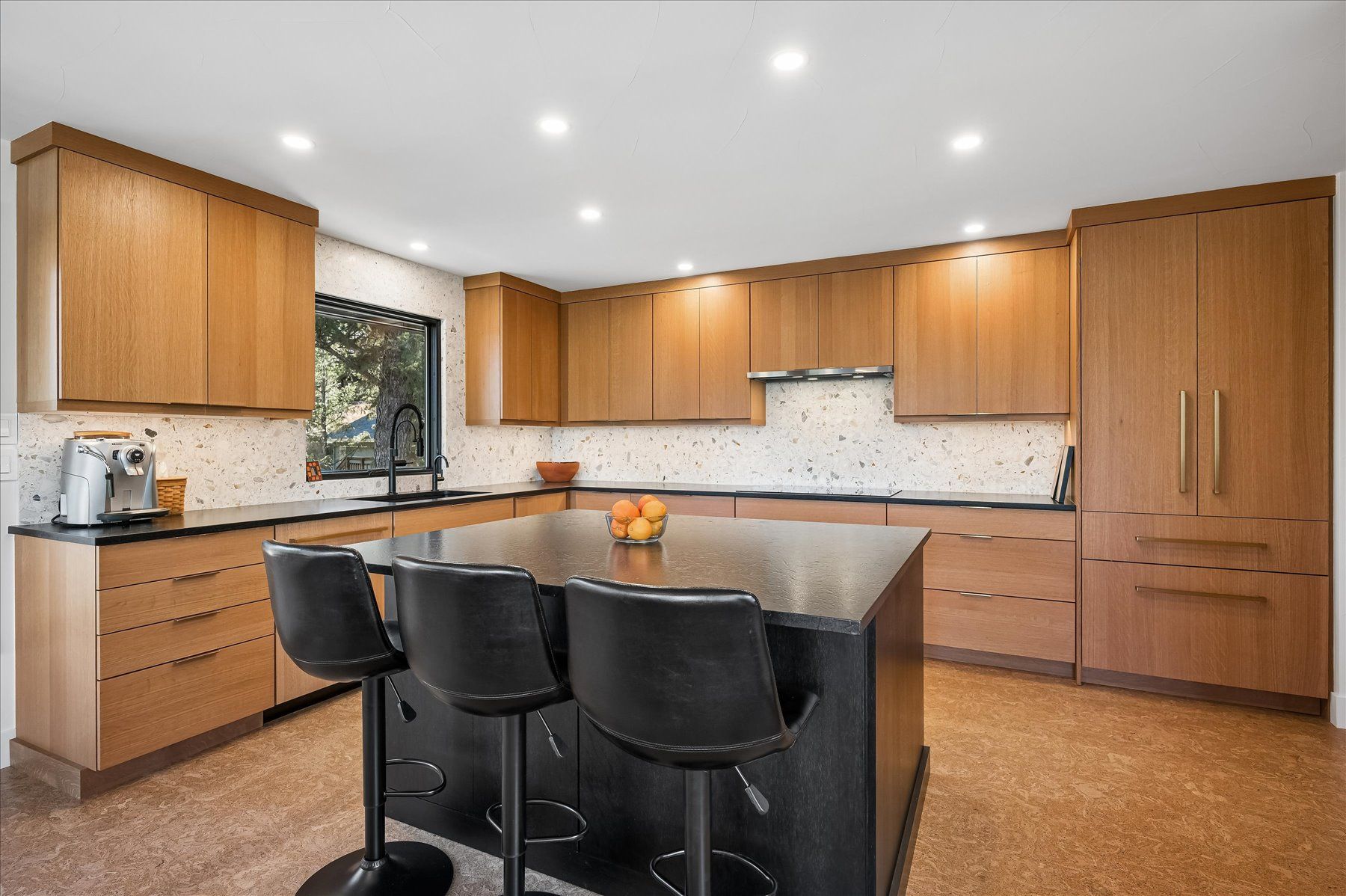 Modern kitchen with wood cabinets, granite island, black stools, and stainless appliances