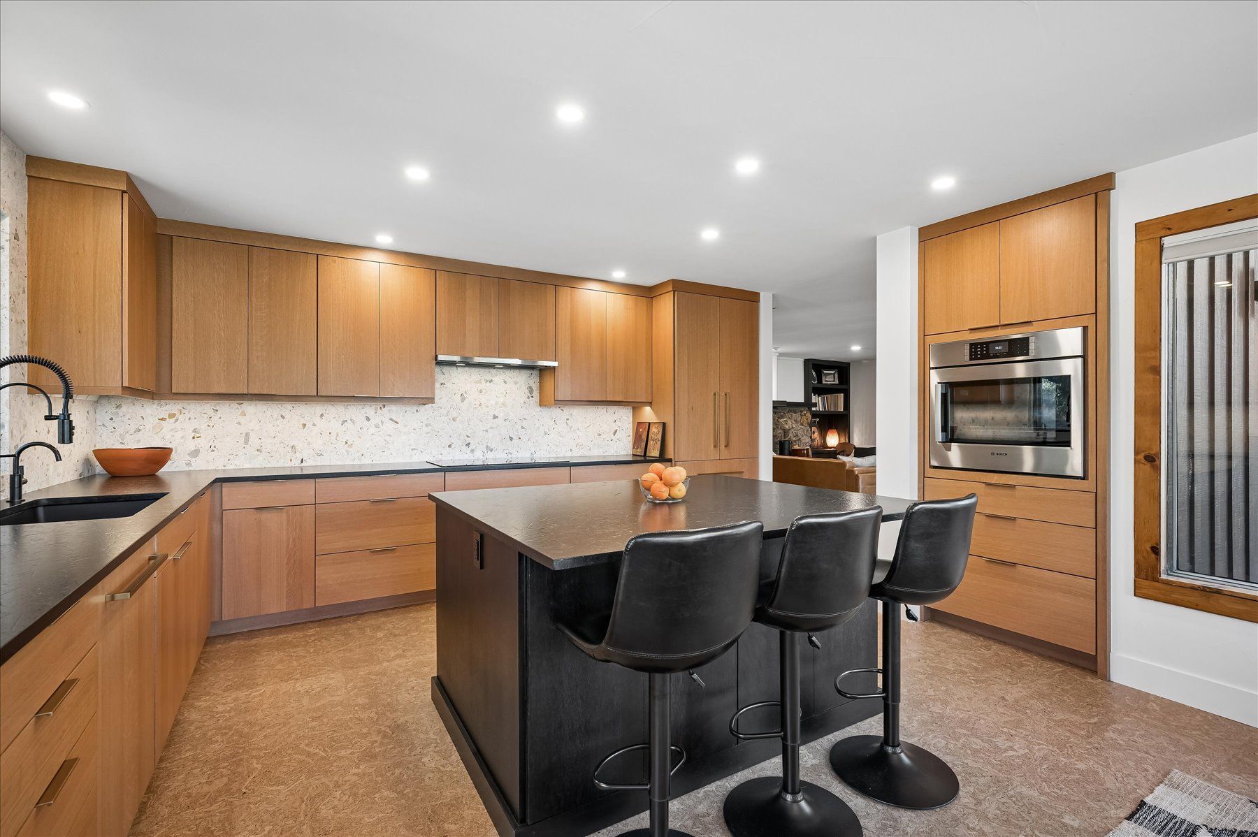 Modern kitchen with wood cabinets, black island stools, stainless appliances, and recessed lighting