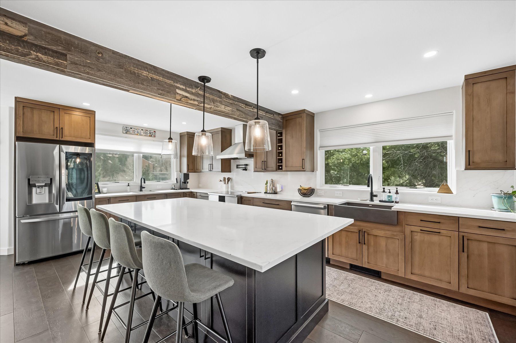Bright modern kitchen with white island, gray stools, wood cabinets, and stainless steel appliances