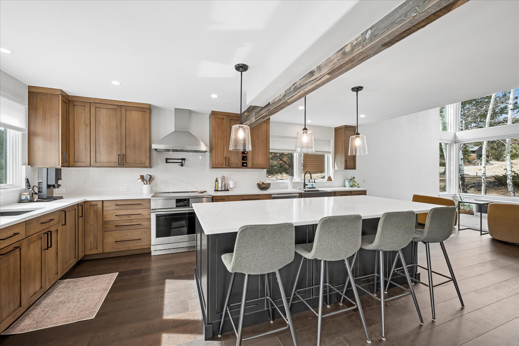 Modern kitchen with wood cabinets, white island, gray barstools, and large windows