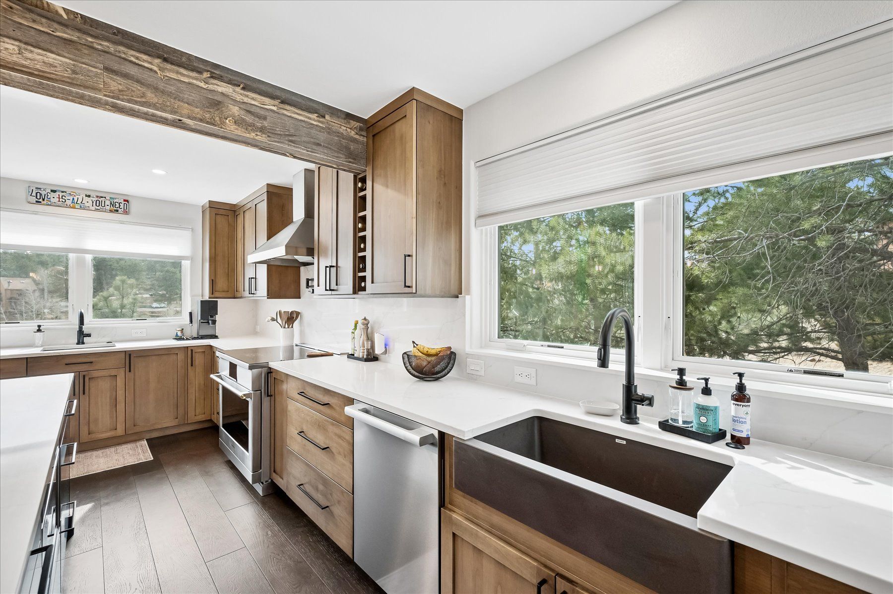 Bright modern kitchen with large windows, wood cabinets, white countertops, and a farmhouse sink