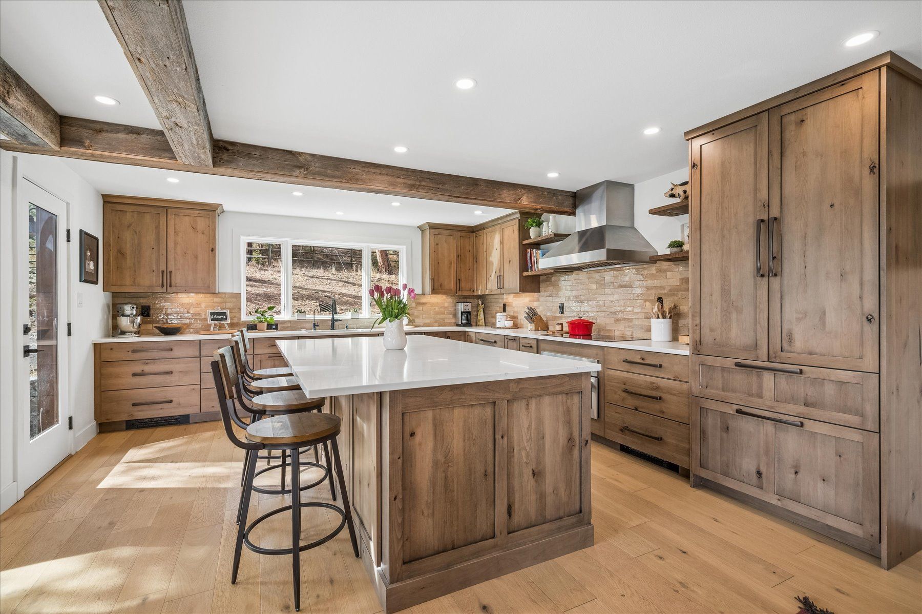 Modern kitchen with wood cabinets, a large island, bar stools, and exposed ceiling beams