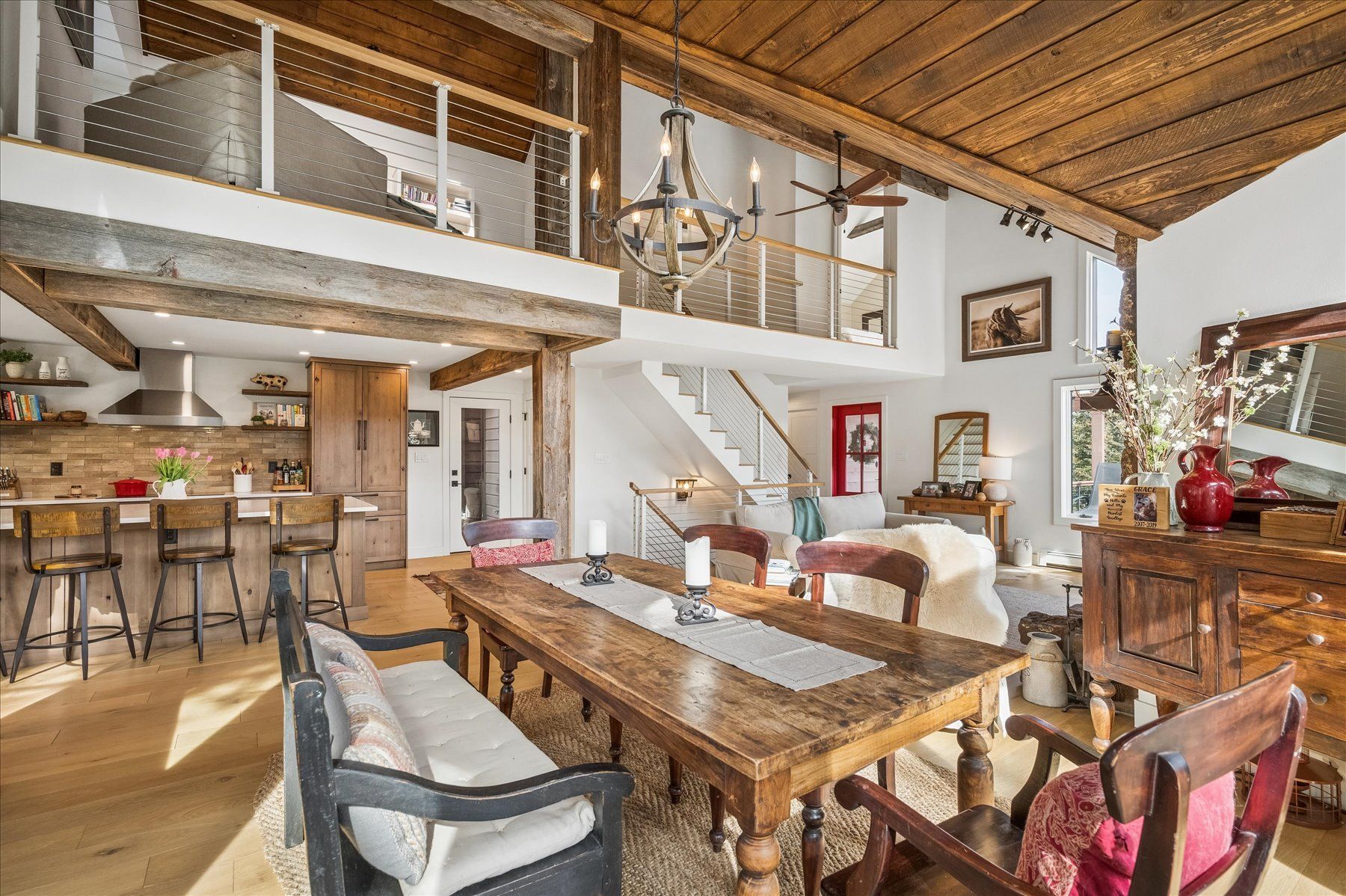 Rustic loft dining room with wooden table, mezzanine, staircase, and stone fireplace