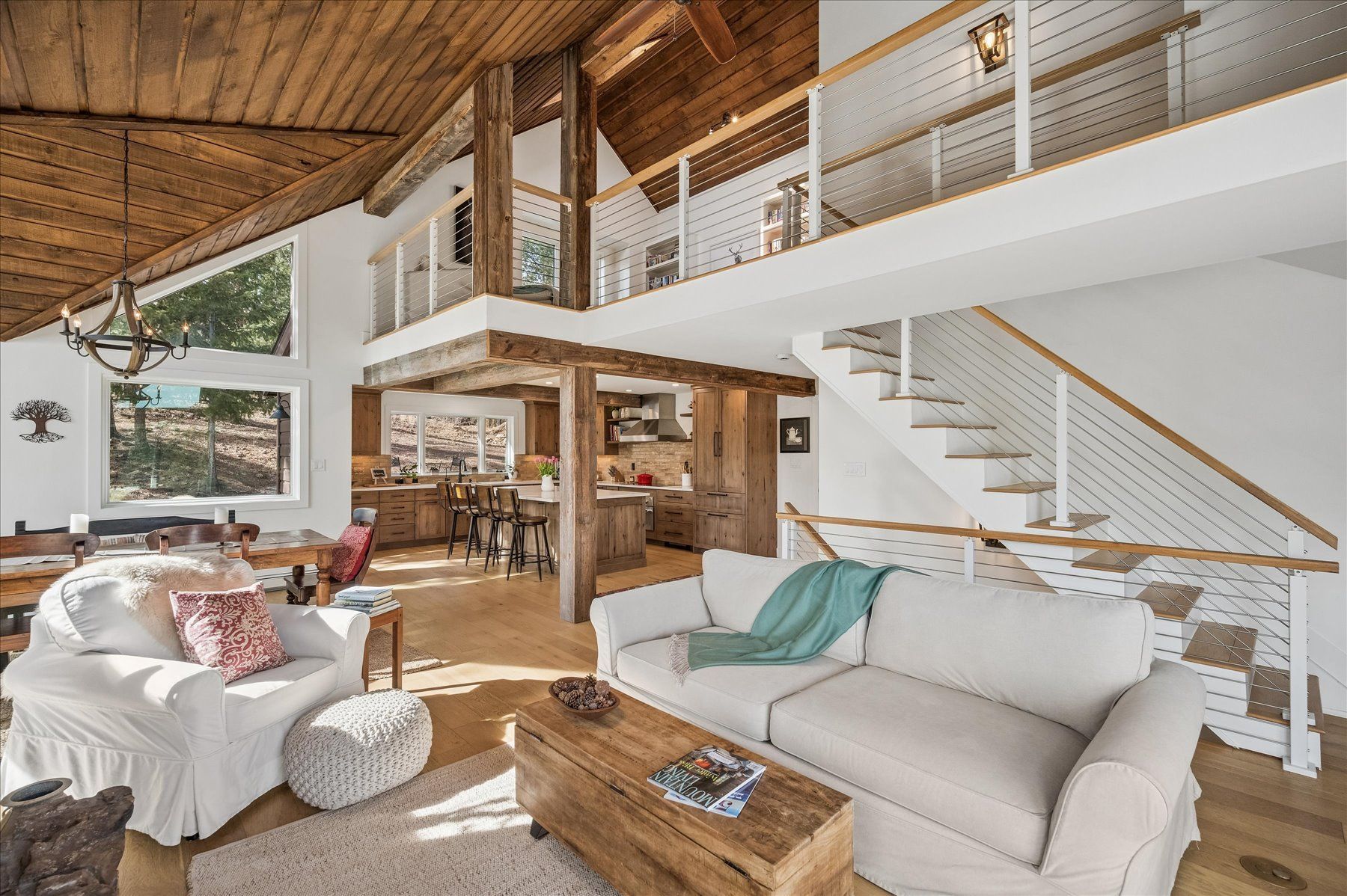 Bright open-plan living room with white sofas, wood accents, high ceilings, and stairs to a loft.