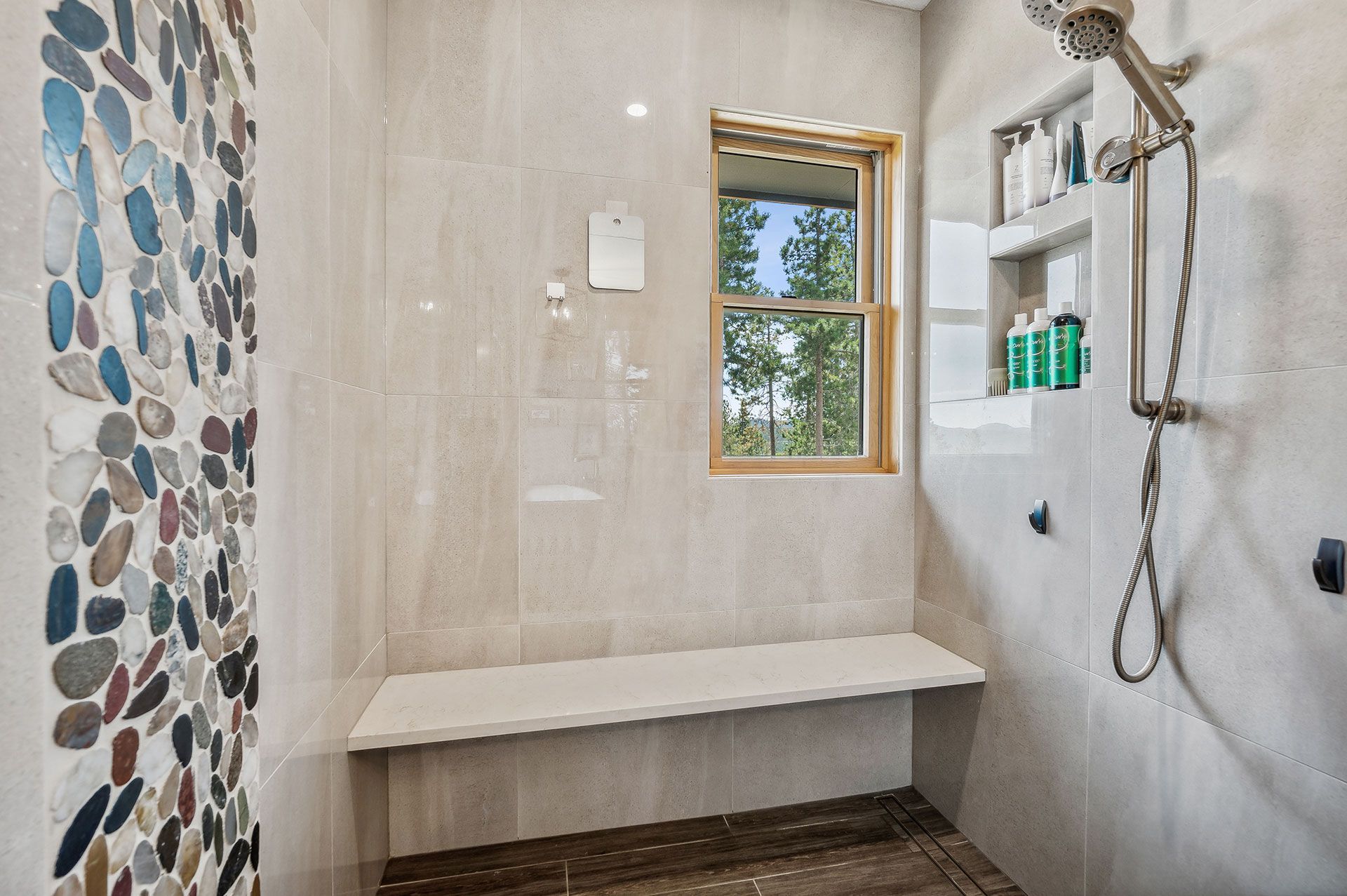 A bathroom with a walk in shower with a bench and a window.
