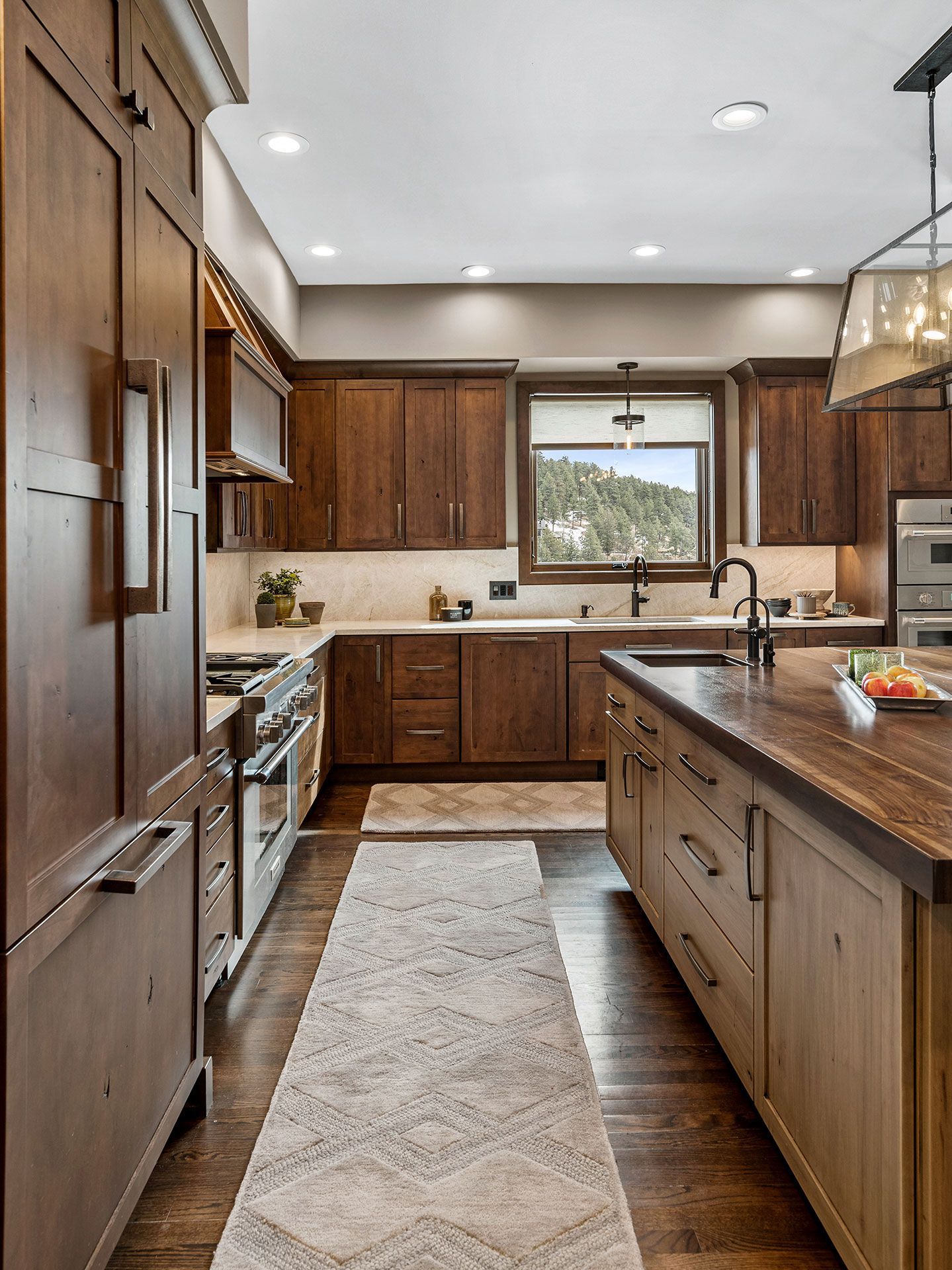 A kitchen with wooden cabinets , granite counter tops , stainless steel appliances and a rug.