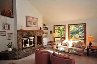 A living room with a fireplace, couch, chairs, and windows.