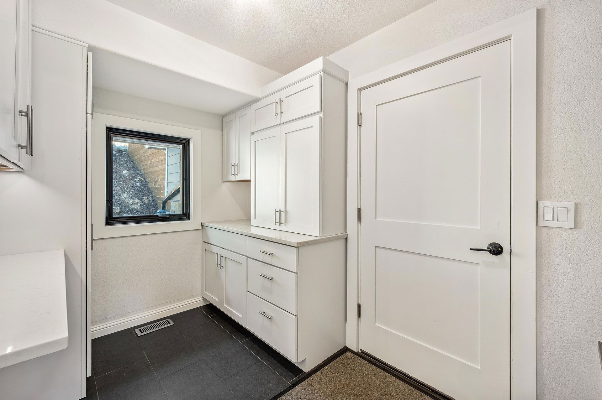 A laundry room with white cabinets and a window.