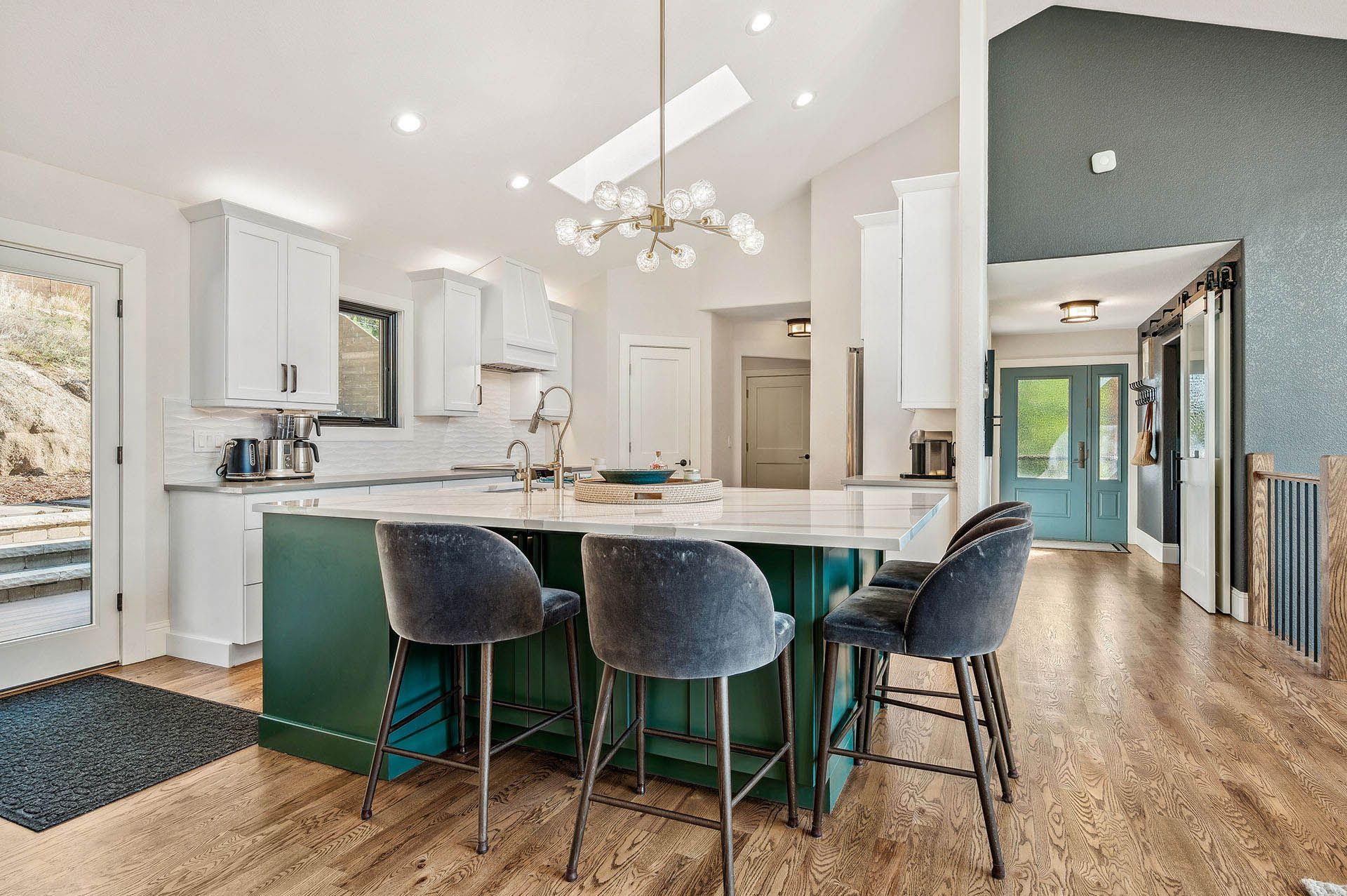 A kitchen with a green island and gray chairs