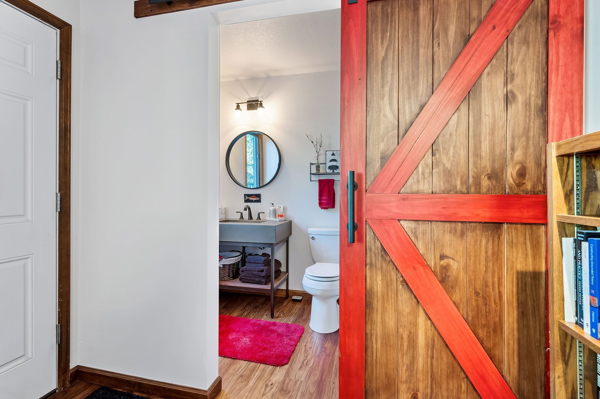 A bathroom with a red sliding barn door leading to it.