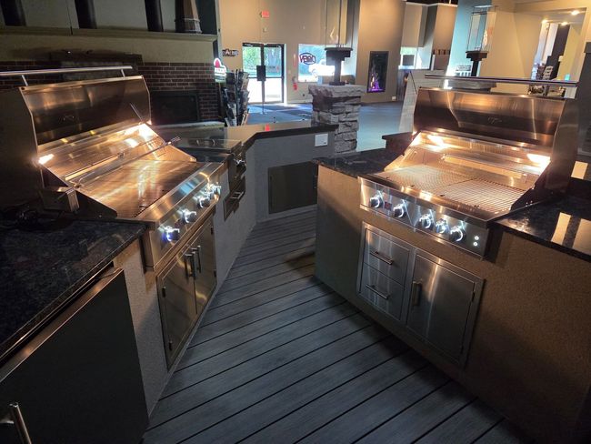 Outdoor patio with a built-in stainless steel grill and outdoor kitchen cabinets under a brick wall.
