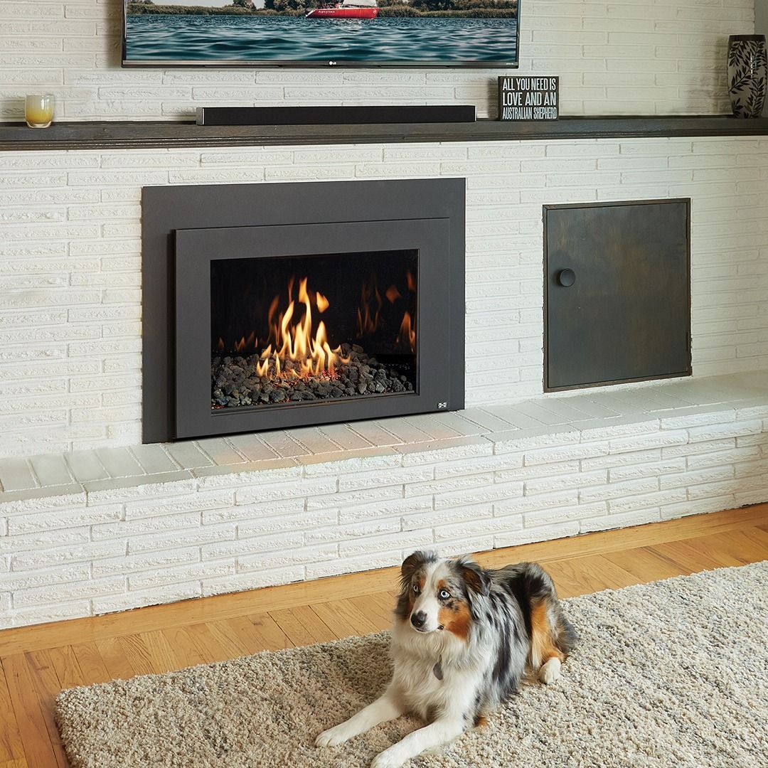 Dog lying on rug in front of a fireplace with burning flames; white brick surround.