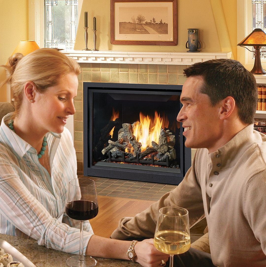 Couple smiling, holding glasses, by a fireplace with flames.