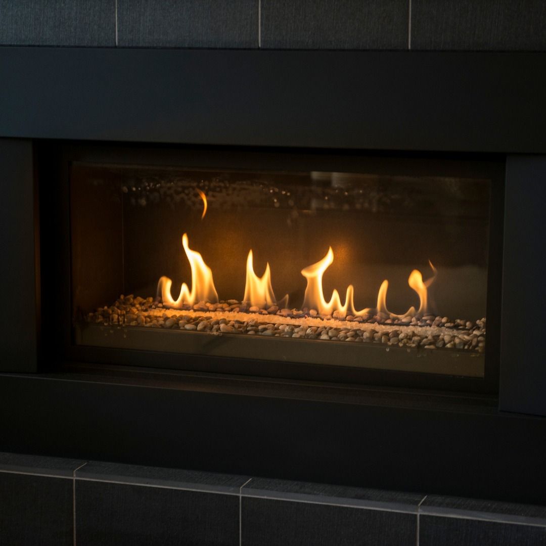 Fireplace with flames and decorative rocks, framed by black trim against dark tiles.