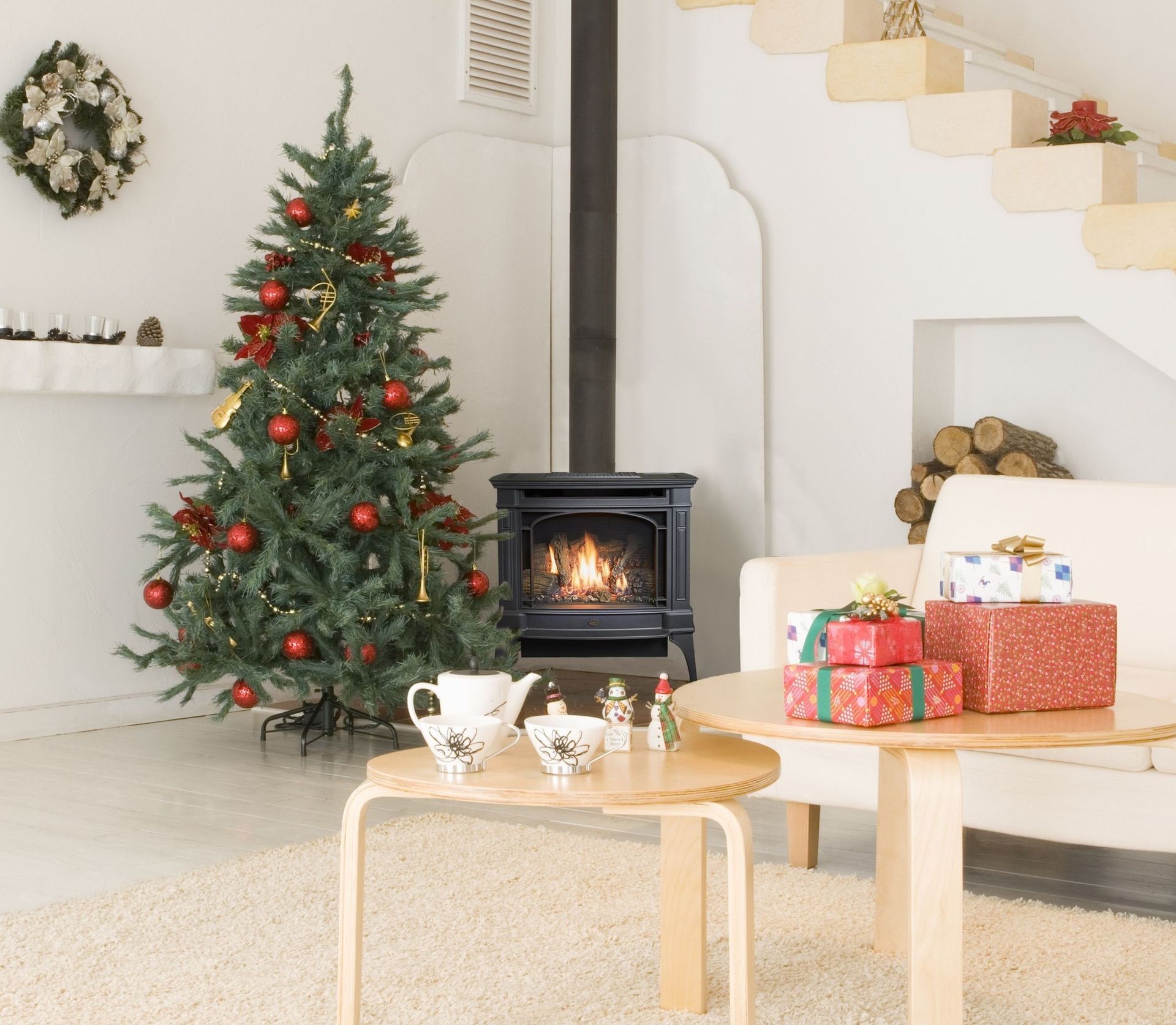 Christmas-decorated living room with tree, fireplace, gifts, and a tea set on a table.