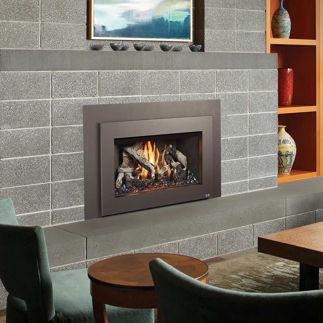 Fireplace with flames and decorative logs, set in a stone wall, in a room with furniture and shelves.