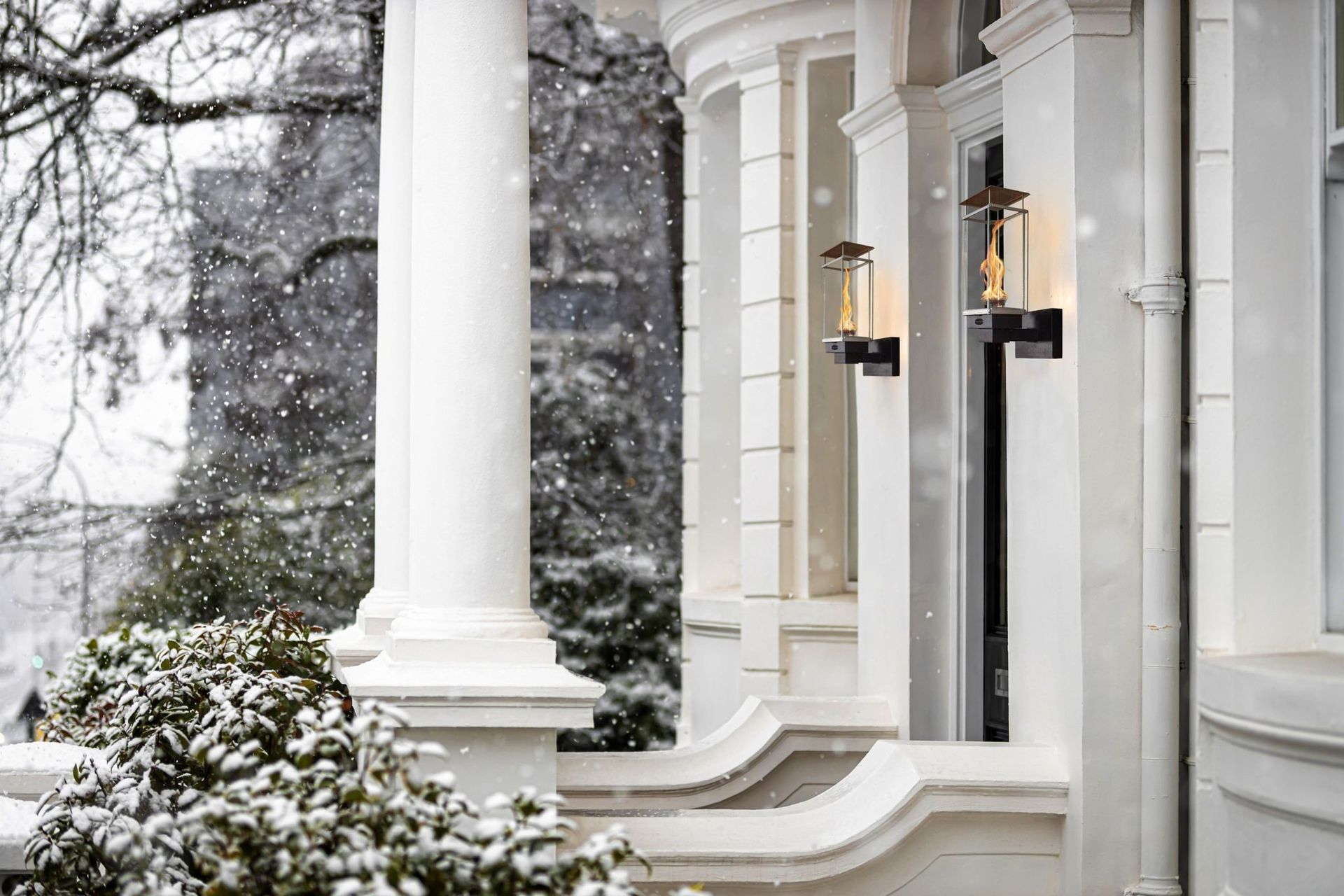 Snowy house exterior with white columns and sconce lights.