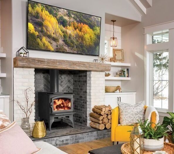 Living room with wood-burning stove, TV, brick fireplace, wooden mantle, and yellow accent chair.