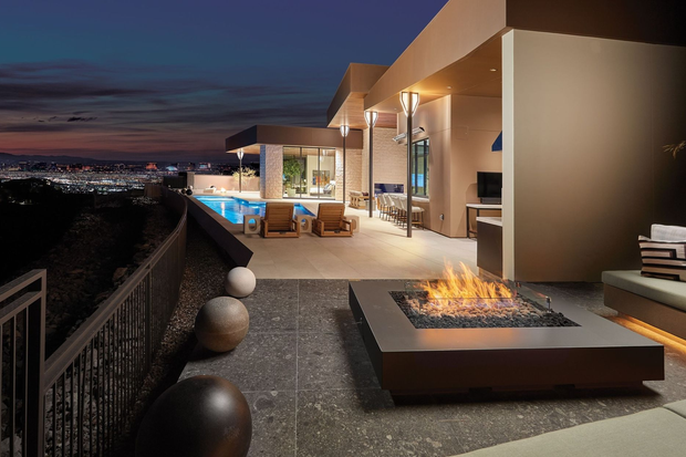 Patio with fire pit, pool, and city view at dusk. Modern home exterior with warm lighting.