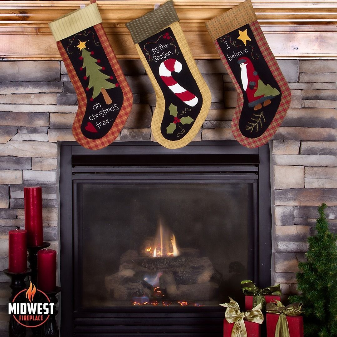 Three Christmas stockings hanging above a fireplace with candles and a small tree.