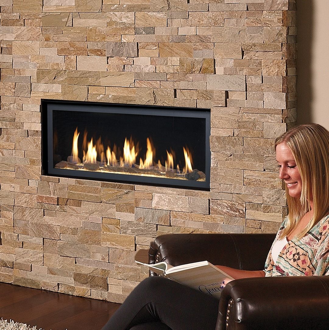 Woman reading by a fireplace with stone surround.