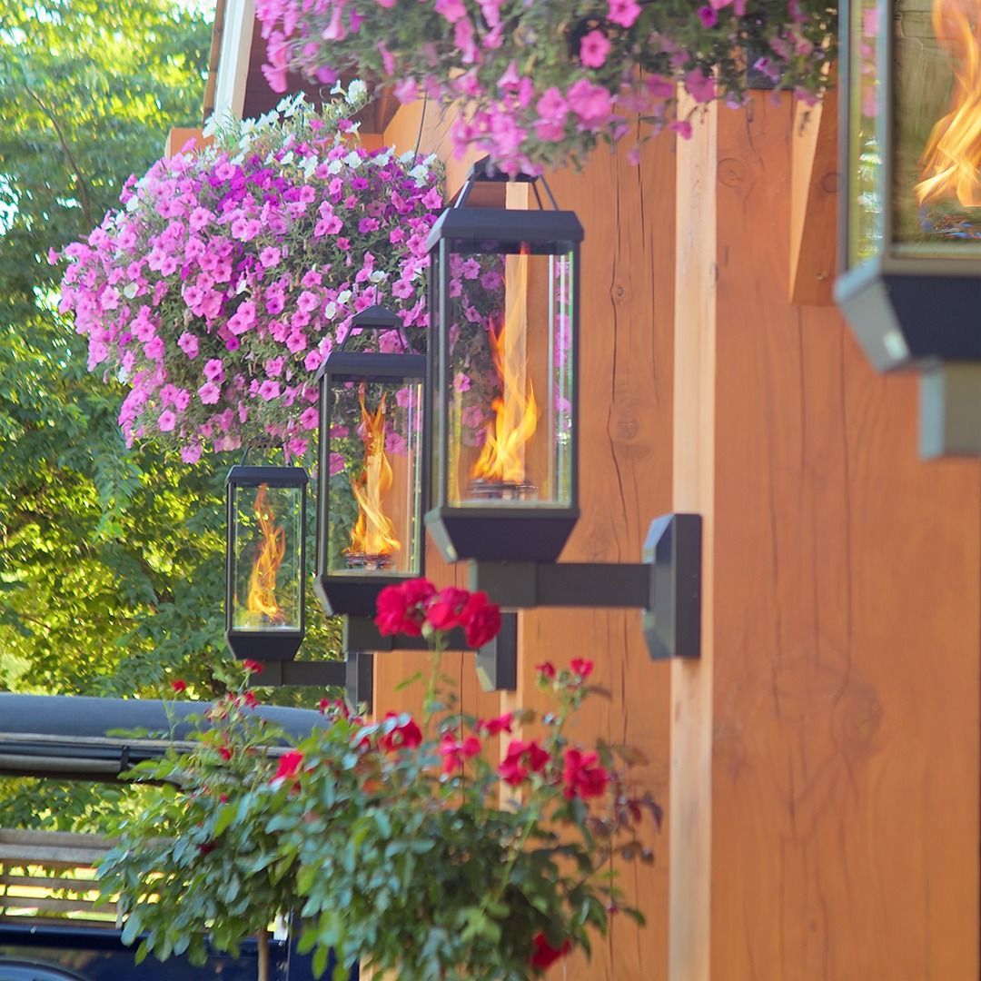 Wall-mounted lanterns with flames, surrounded by flowers, on a wooden structure.