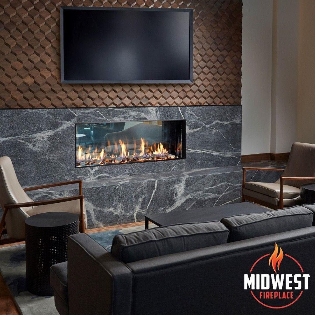Modern living room with fireplace, TV, seating. Dark marble, gray couch, dark wood accents.