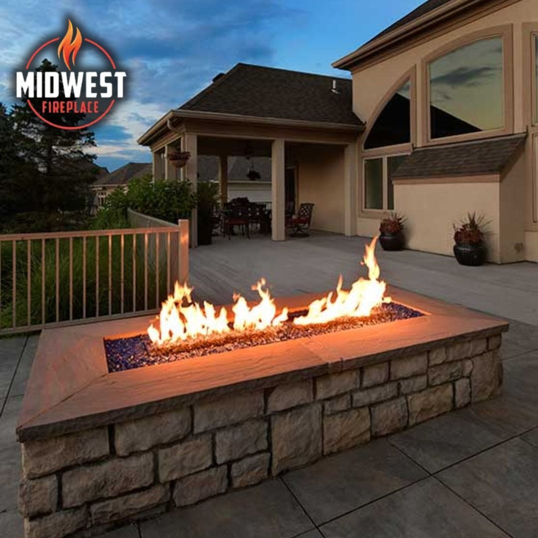 A lit gas fire pit with stone veneer in an outdoor patio setting.