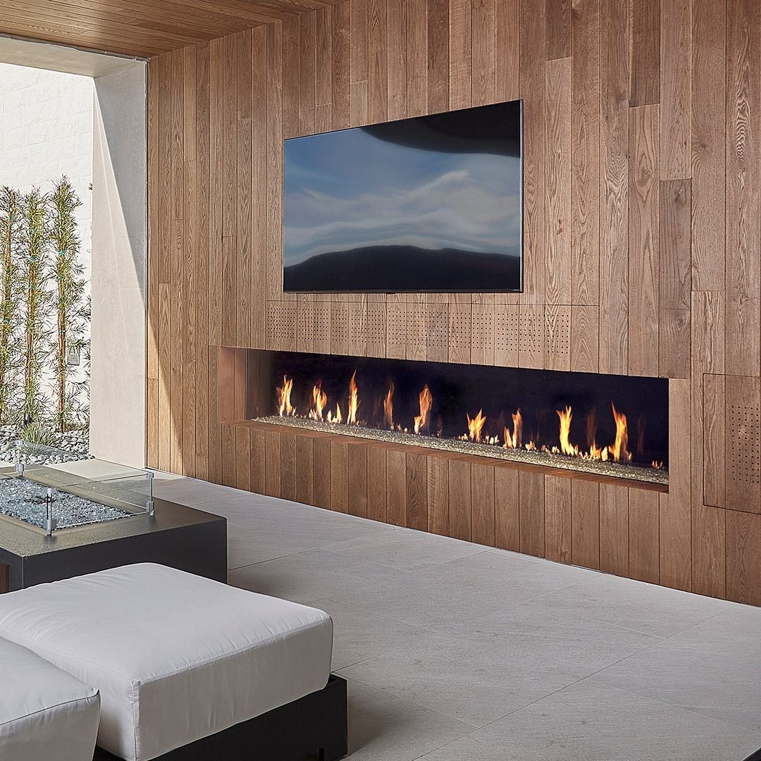 Fireplace with flames below a TV set on a wood-paneled wall, outdoor seating visible.