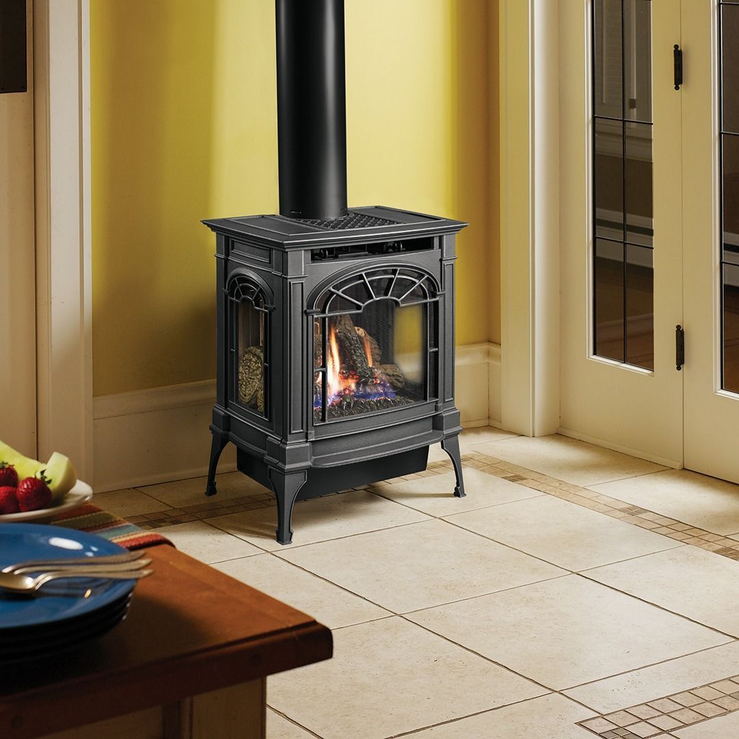 Gas stove with a black chimney in a corner of a room, tile floor, open glass doors visible.