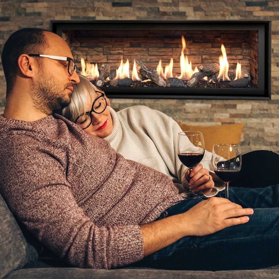 Couple cuddling on a couch, enjoying wine, with a fireplace in the background.