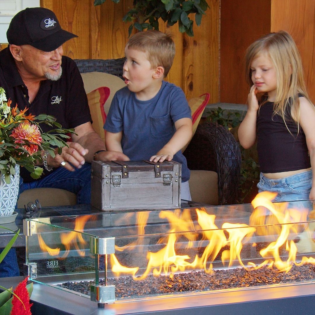 Man with two children looks at a glowing fire pit outdoors.