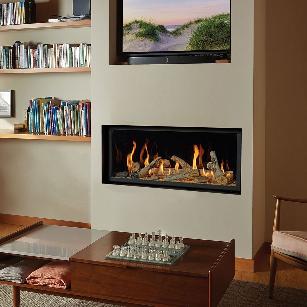 Fireplace with burning logs, built into a neutral-colored wall with TV above. Bookshelf to the left, and a coffee table with chess set below.