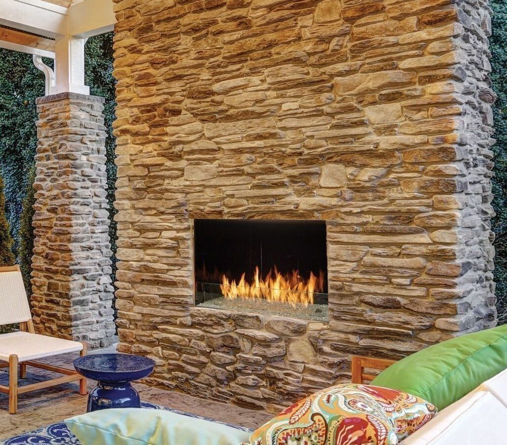 Outdoor stone fireplace with flames, next to a seating area with cushions and a small blue table.