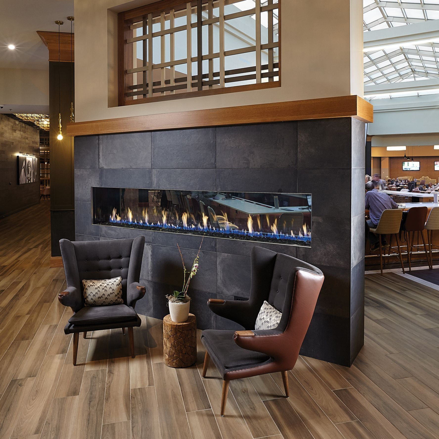 Two armchairs face a fireplace in a hotel lobby. Fireplace is on a dark stone wall.