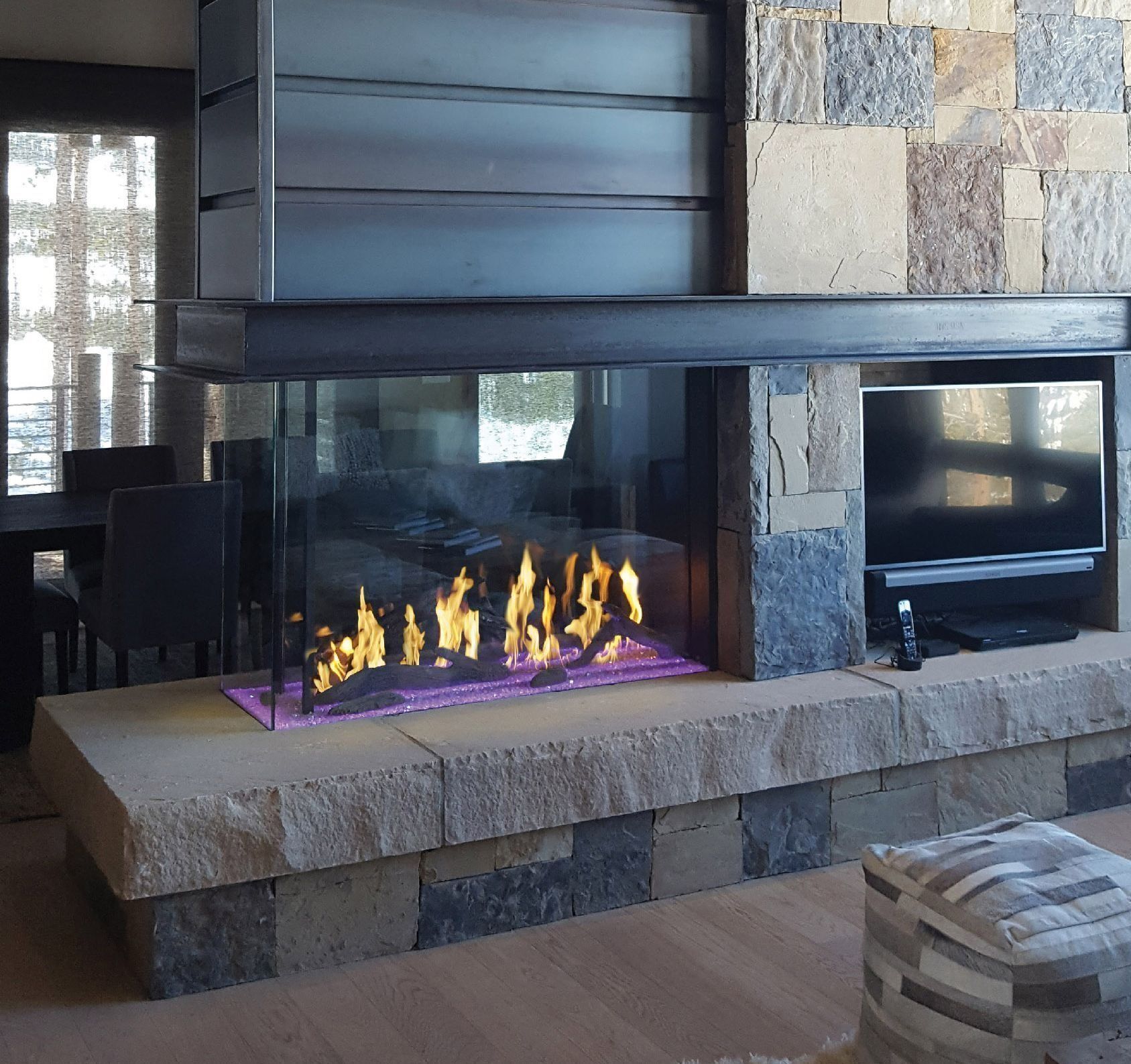 Modern stone fireplace with glass sides, flames, and built-in TV.