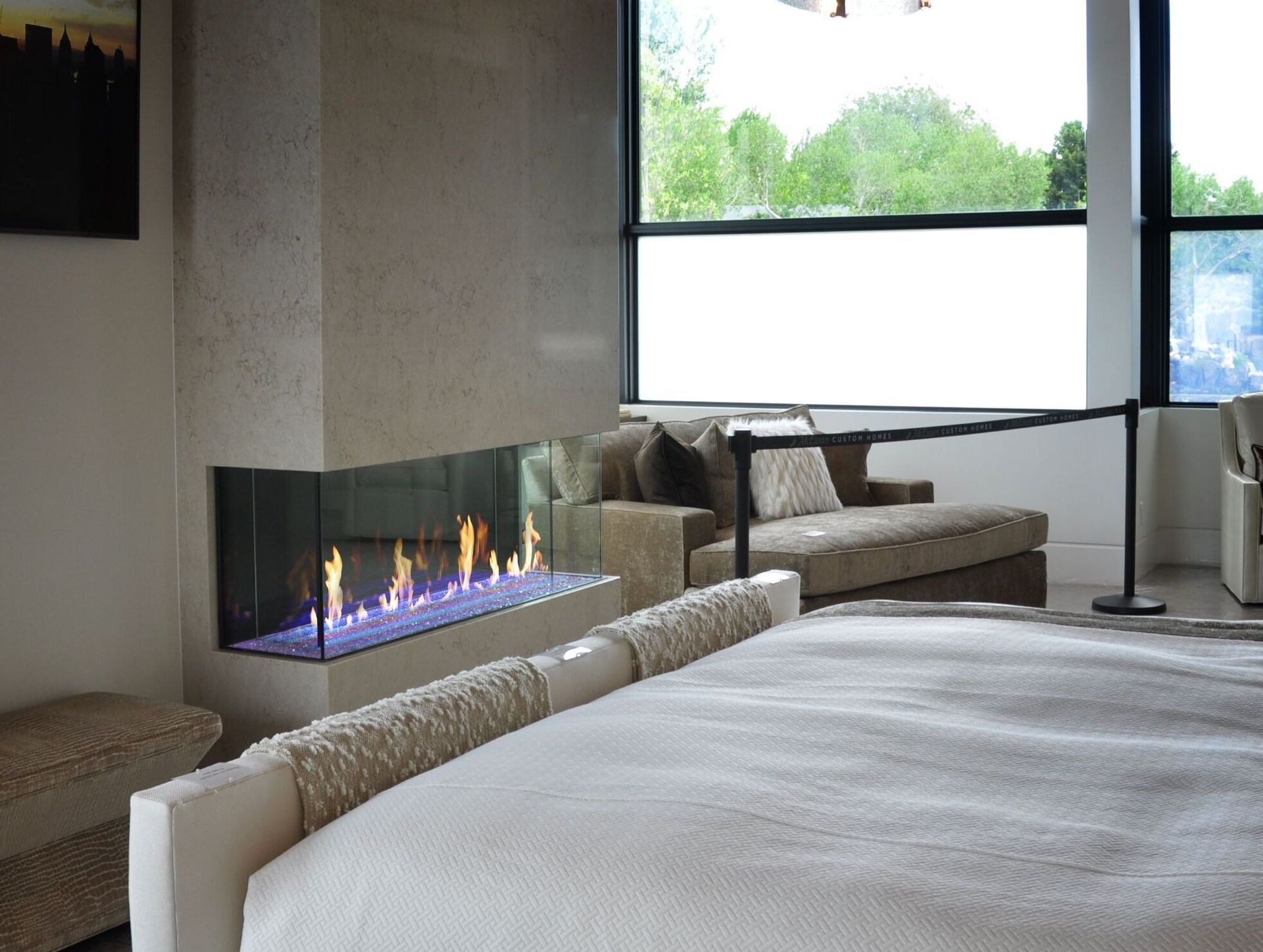 Modern bedroom with a fireplace and large windows overlooking trees.