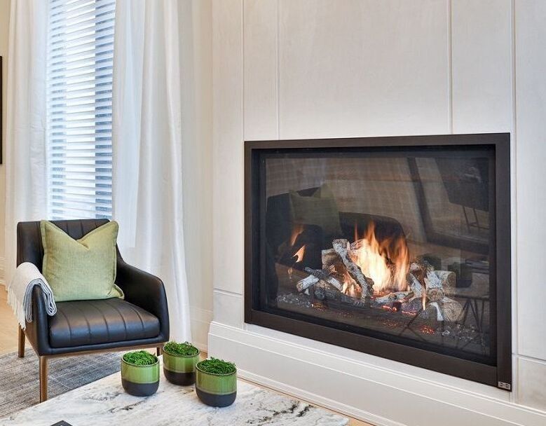 Fireplace with burning flames, a dark chair with a green pillow, and small potted plants.