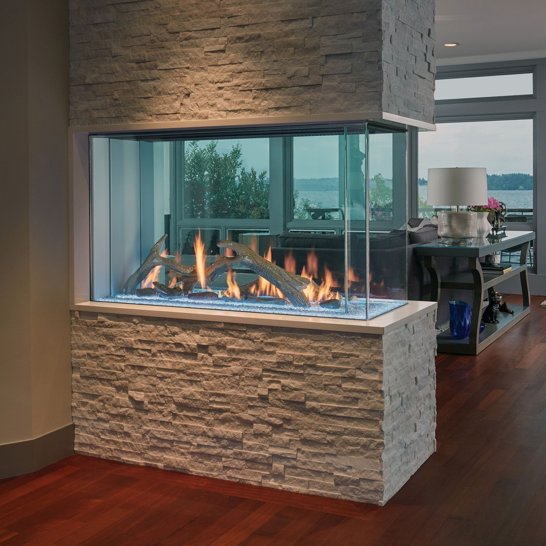 Modern corner fireplace with stone surround, glass sides, and visible flames.