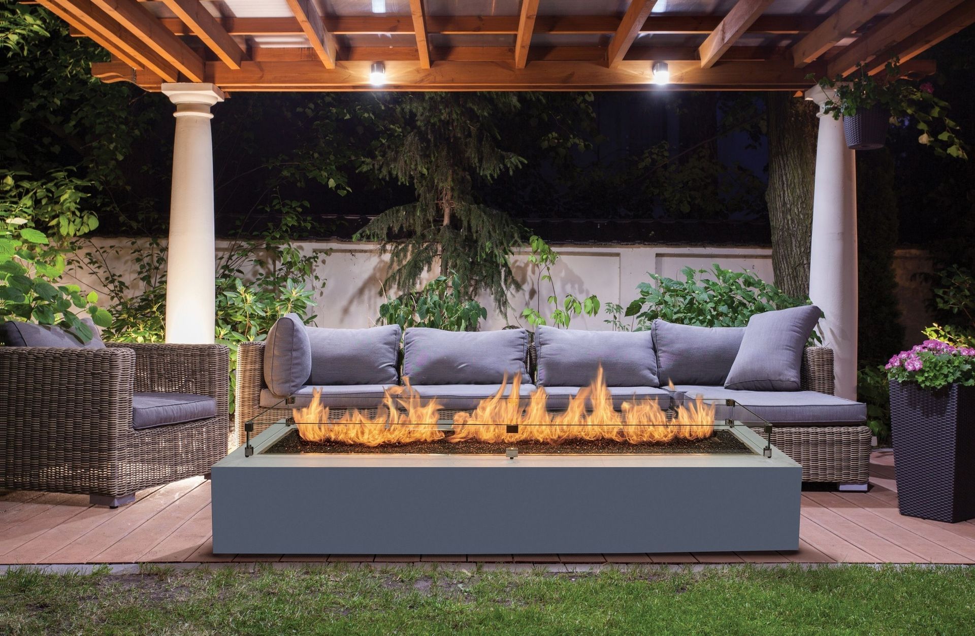 A patio with a fire pit, couch, and seating under a pergola at night.