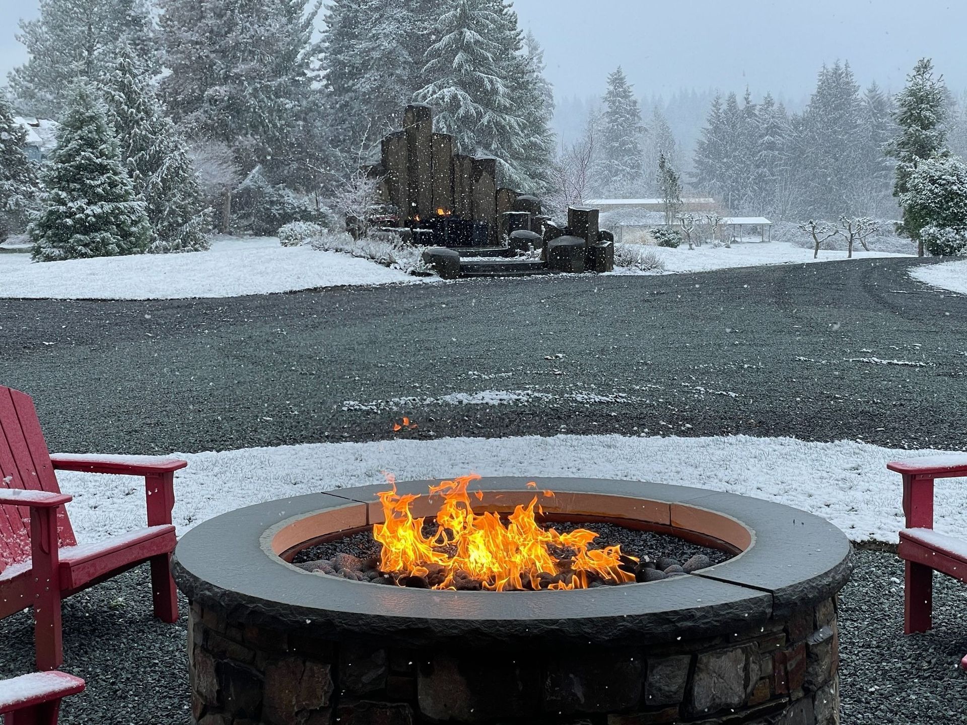 Fire pit with flames, two red chairs, and a snowy landscape with trees.