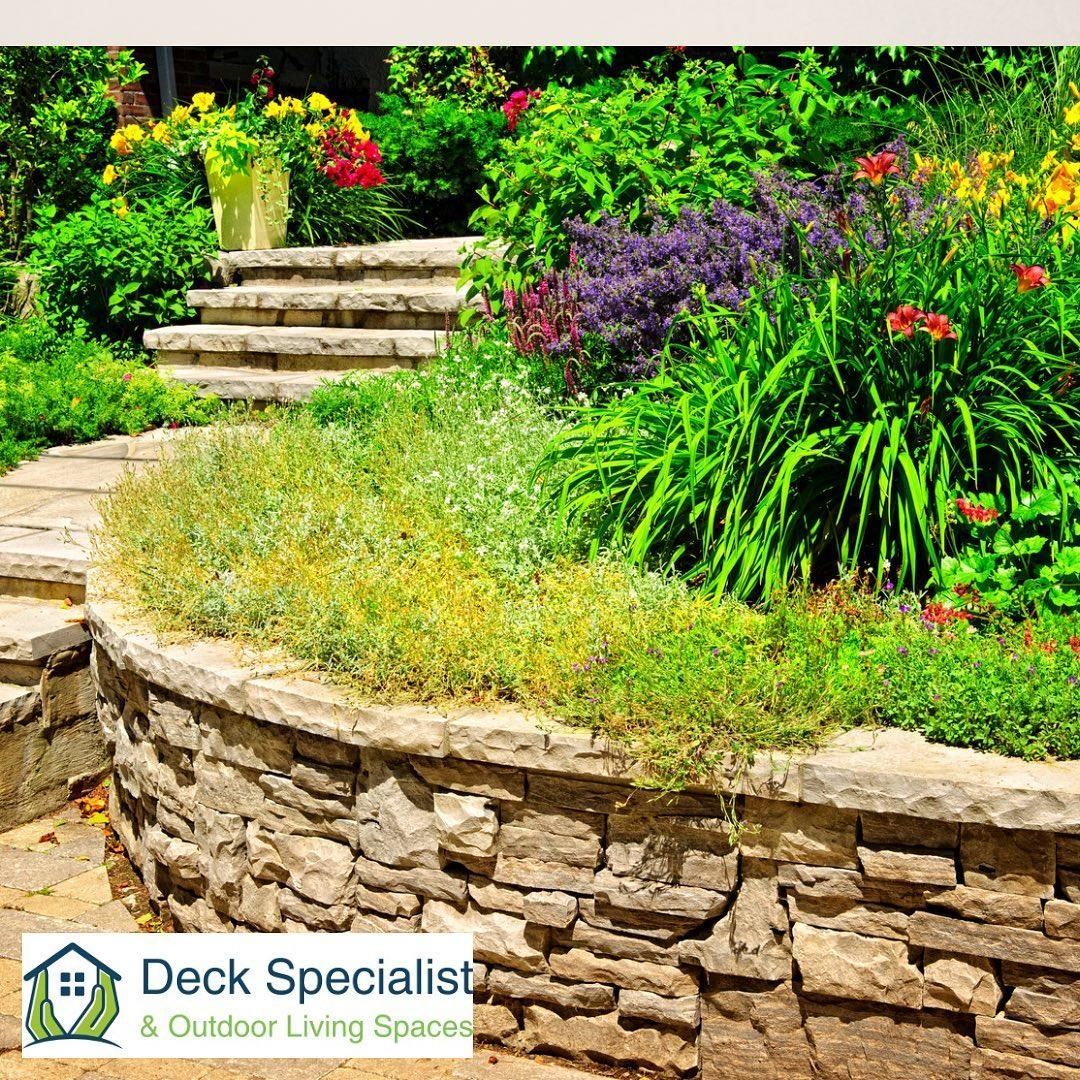 A stone wall surrounds a garden with flowers and stairs.