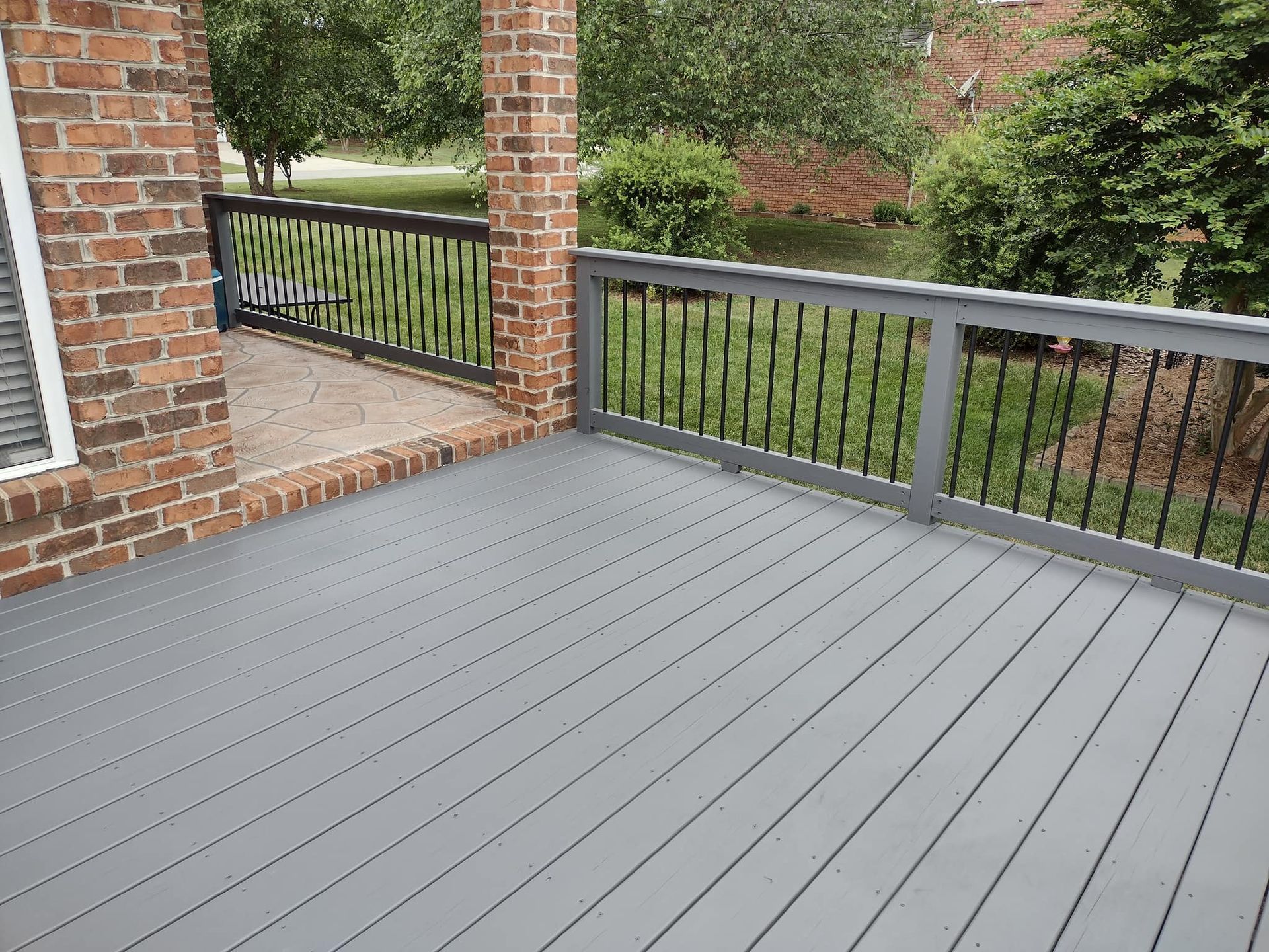 A gray deck with a metal railing and a brick building in the background.