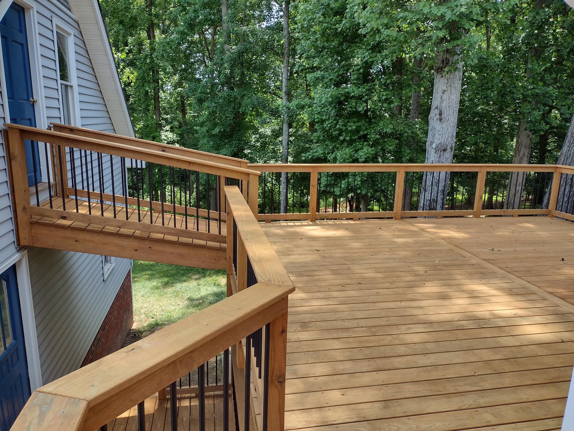A large wooden deck with stairs leading up to it is surrounded by trees.