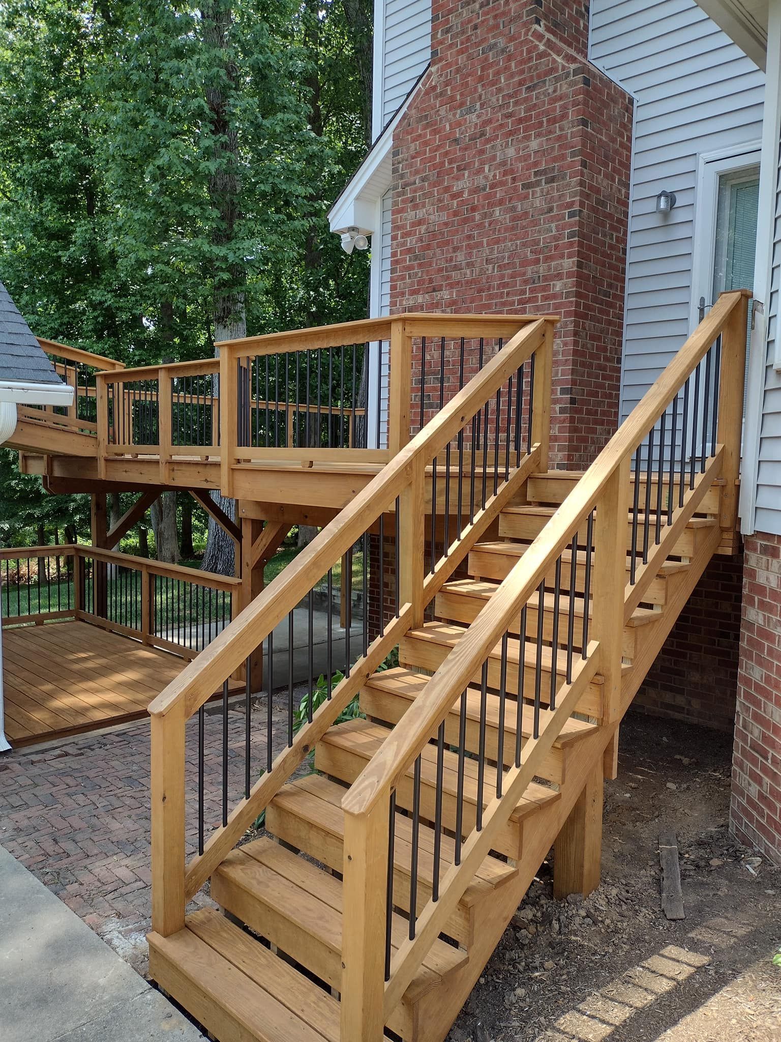 A wooden deck with stairs leading up to it next to a brick house.