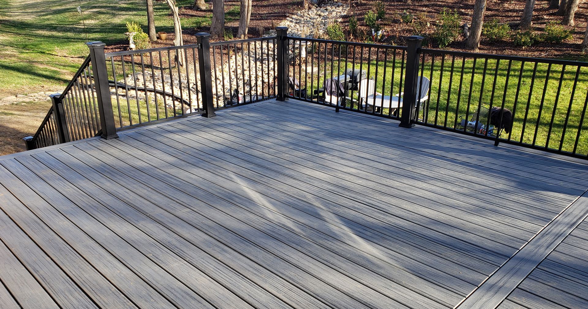 A wooden deck with a metal railing and chairs on it.