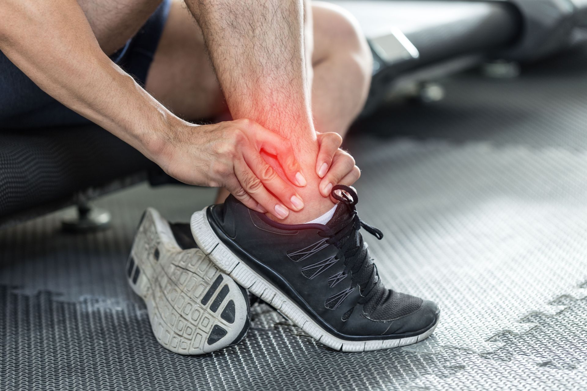 A man is holding his ankle in pain while sitting on a treadmill.
