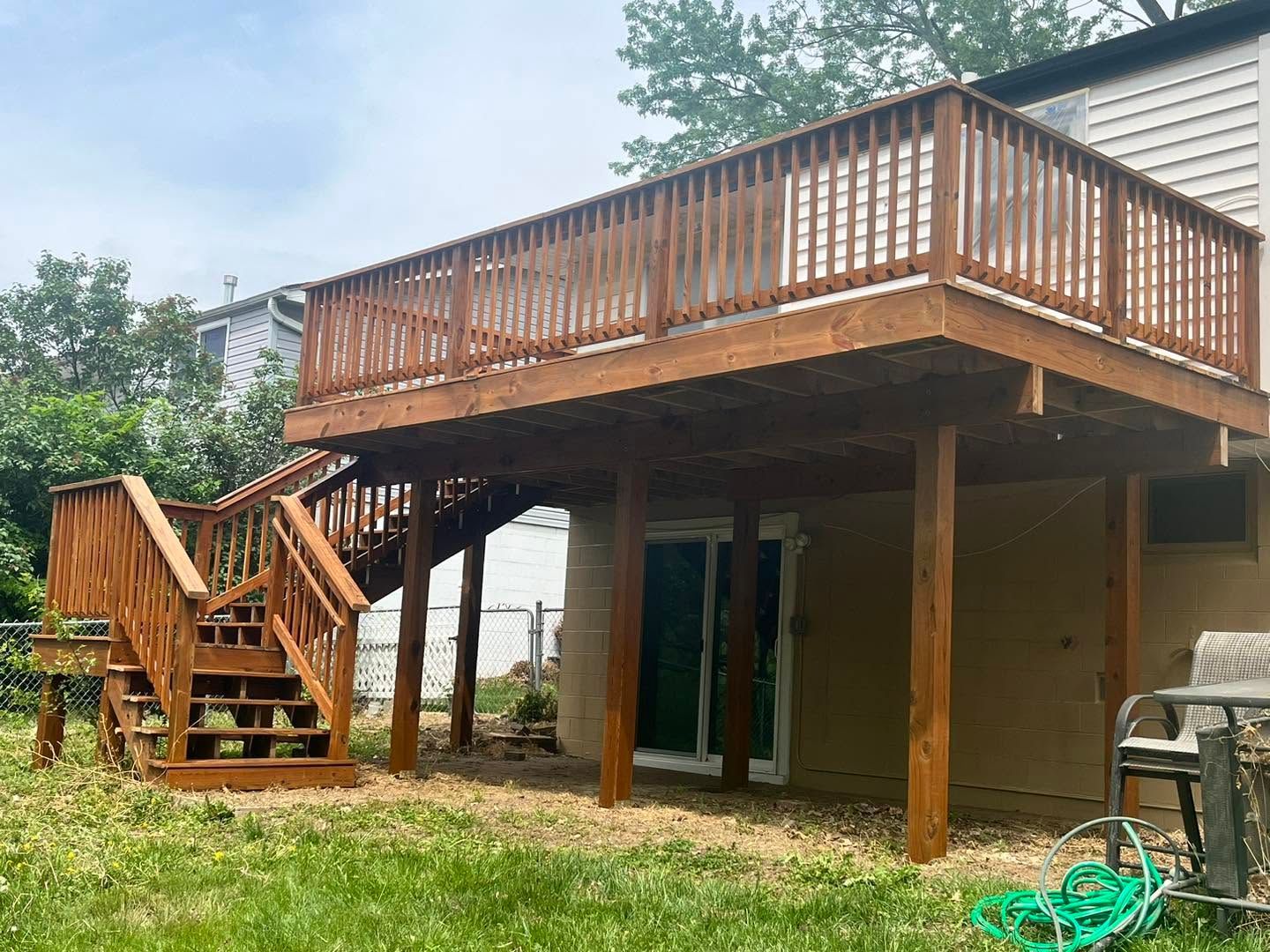 Backyard deck on stilts with wooden stairs and railing beside a house on a grassy lawn