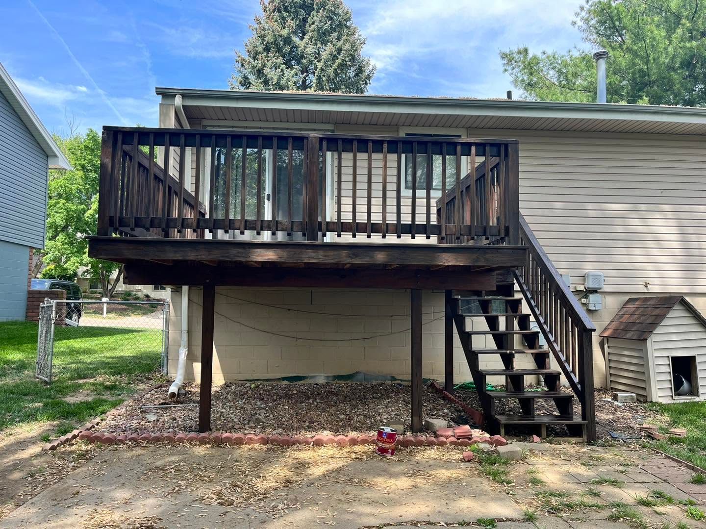 Back deck with stairs on a beige house, supported by posts over a gravel area.