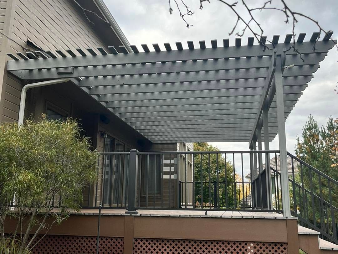 Outdoor patio with a metal pergola, railing, and potted shrubs beside a building